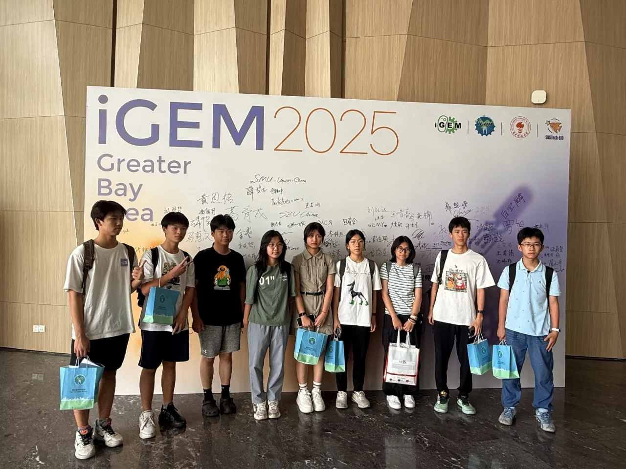 The GCGS iGEM team standing in front of an iGEM 2025 Greater Bay Area banner.